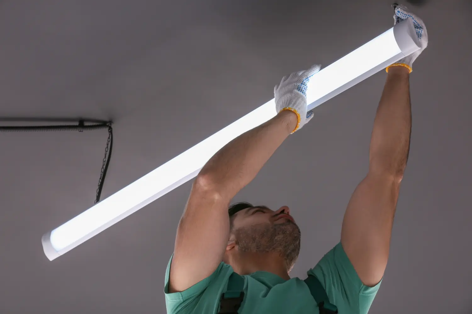 Deckenleuchte. Elektriker installiert lineare LED-Lampe im Innenbereich, Blick aus dem niedrigen Winkel
